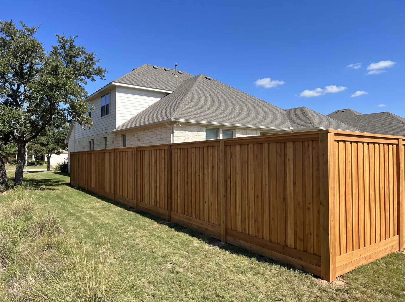 A board-on-board cedar privacy fence with a kickboard and a cap and trim along the side yard of a limestone house